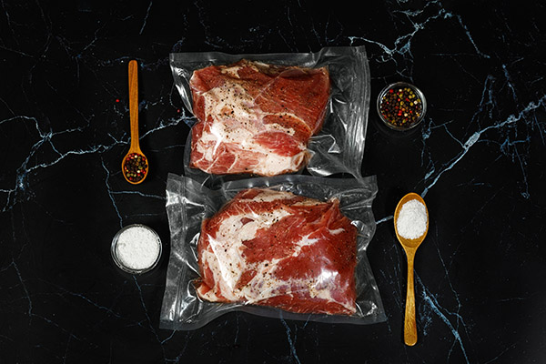 A hús vákuumcsomagolt fűszerekkel és sóval fekete alapon.